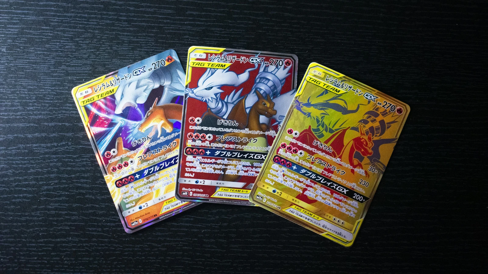 Tres cartas Pokémon japonesas con distintas versiones de la misma pareja de personajes sobre una mesa oscura